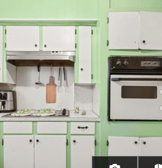 kitchen with light countertops, decorative backsplash, oven, and under cabinet range hood