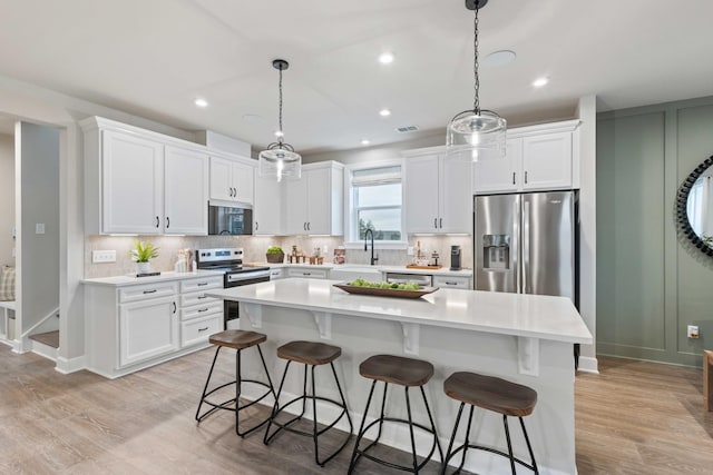 kitchen with a breakfast bar, stainless steel appliances, tasteful backsplash, light wood-style flooring, and white cabinetry