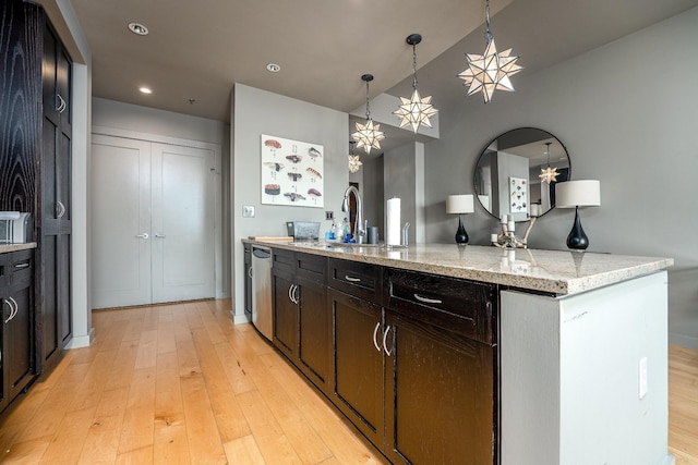 kitchen with stainless steel dishwasher, a sink, light stone counters, and light wood-style floors