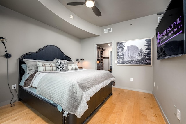 bedroom with ceiling fan, light wood-style flooring, visible vents, baseboards, and a walk in closet