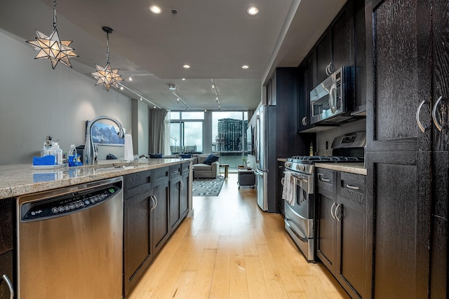 kitchen with open floor plan, decorative light fixtures, stainless steel appliances, a wall of windows, and light wood-style floors