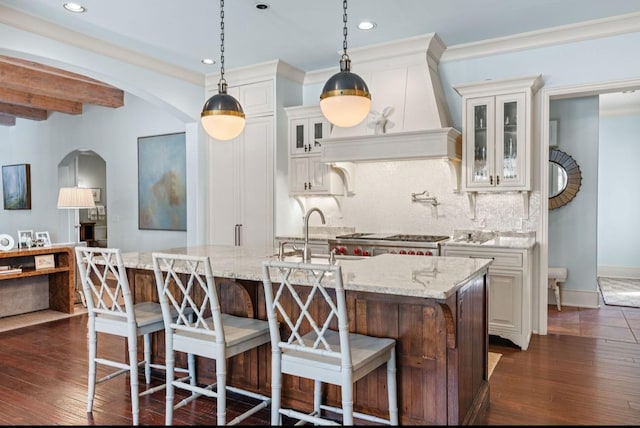 kitchen with arched walkways, custom range hood, decorative backsplash, dark wood-type flooring, and a sink