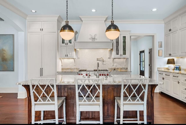 kitchen featuring premium range hood, dark wood-style flooring, a breakfast bar, glass insert cabinets, and crown molding