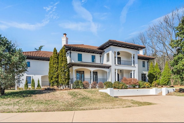 mediterranean / spanish-style house with a tile roof, a chimney, stucco siding, a front yard, and a balcony