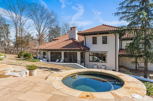 rear view of house with a patio, a sunroom, a chimney, a tiled roof, and an in ground hot tub