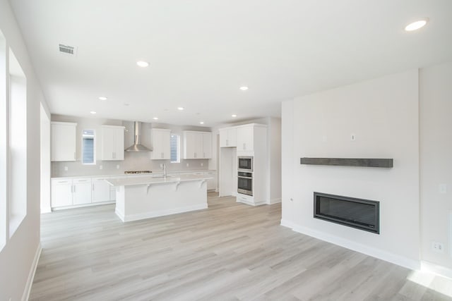 kitchen with visible vents, light wood-style floors, a glass covered fireplace, white cabinets, and wall chimney range hood