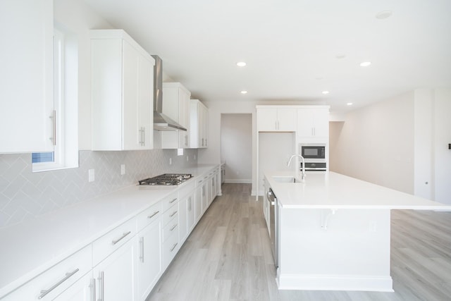 kitchen featuring stainless steel gas cooktop, a sink, wall chimney range hood, black microwave, and backsplash