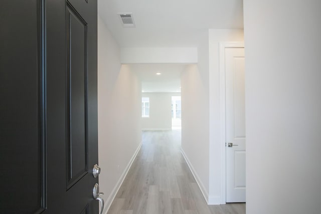 hall with visible vents, light wood-style flooring, and baseboards