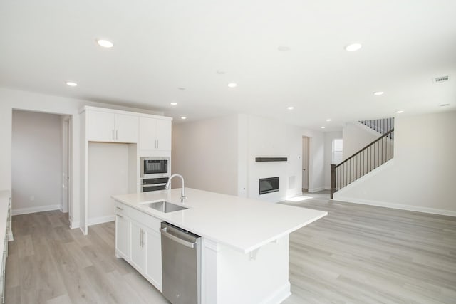 kitchen featuring a glass covered fireplace, appliances with stainless steel finishes, light wood-style floors, a sink, and recessed lighting