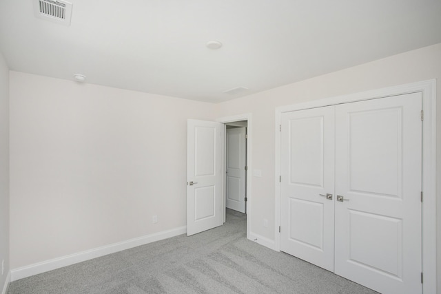 unfurnished bedroom with a closet, light colored carpet, visible vents, and baseboards