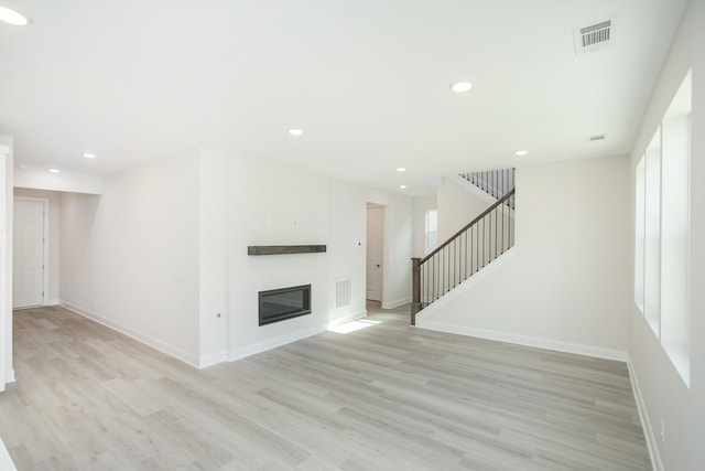 unfurnished living room featuring recessed lighting, visible vents, stairs, light wood-type flooring, and a glass covered fireplace