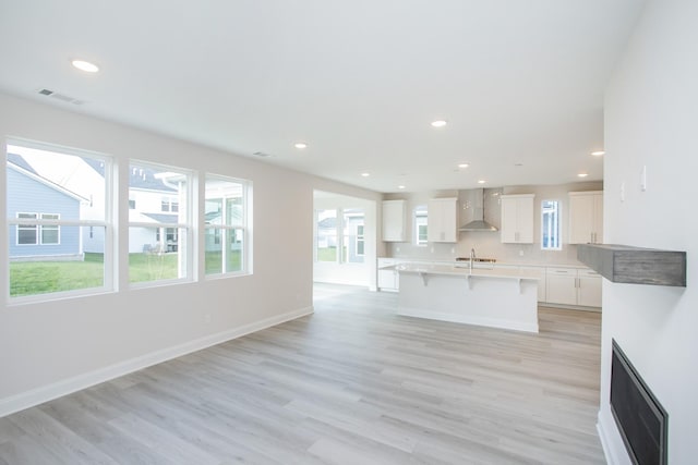 kitchen featuring a center island with sink, light wood finished floors, wall chimney exhaust hood, visible vents, and a kitchen breakfast bar