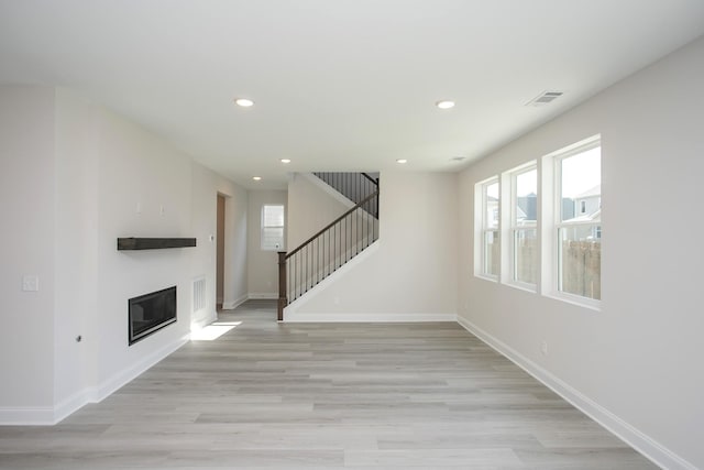 unfurnished living room featuring light wood-style floors, stairs, baseboards, and recessed lighting