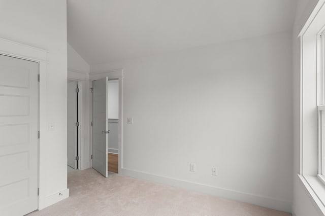 unfurnished bedroom featuring multiple windows, baseboards, vaulted ceiling, and light colored carpet