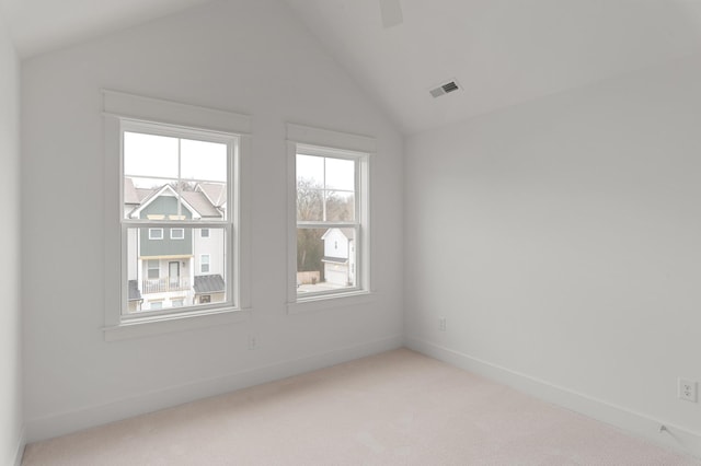 spare room featuring lofted ceiling, baseboards, visible vents, and light colored carpet