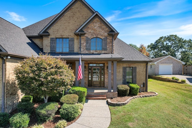 view of front facade with roof with shingles, covered porch, stone siding, an outdoor structure, and a front lawn