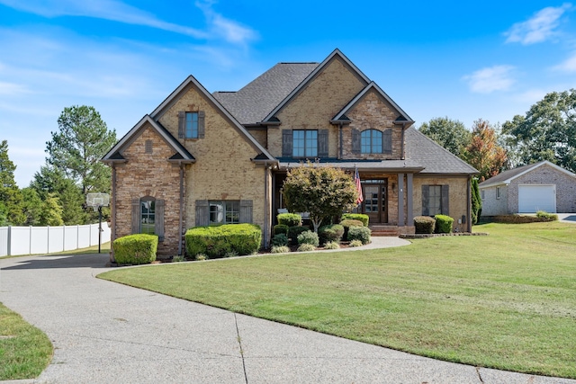 view of front of home with a shingled roof, a front yard, brick siding, and fence