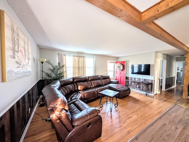 living room featuring a wainscoted wall, a textured ceiling, wood finished floors, and beam ceiling