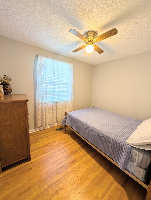 bedroom with ceiling fan, visible vents, a textured ceiling, and light wood-style flooring