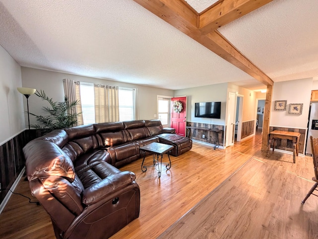 living area with a wainscoted wall, beam ceiling, a textured ceiling, and light wood-style flooring