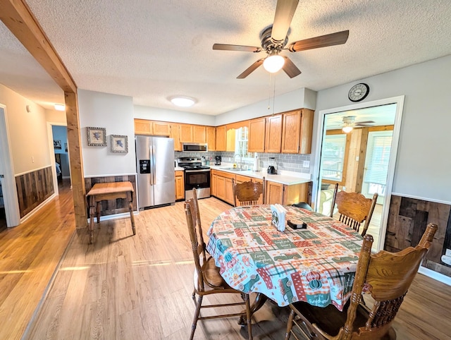 dining room with wooden walls, light wood finished floors, wainscoting, and a healthy amount of sunlight