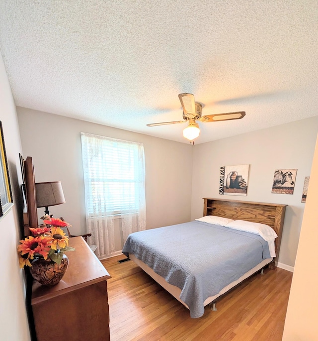 bedroom with a ceiling fan, baseboards, a textured ceiling, and light wood finished floors