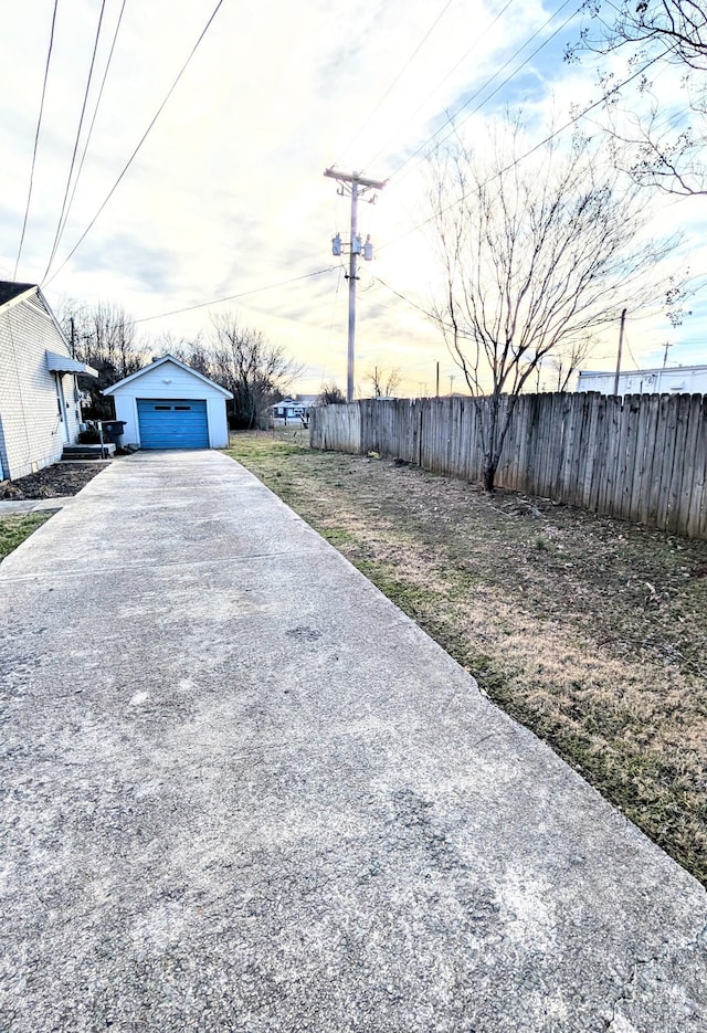 view of yard with a garage, driveway, fence, and an outbuilding