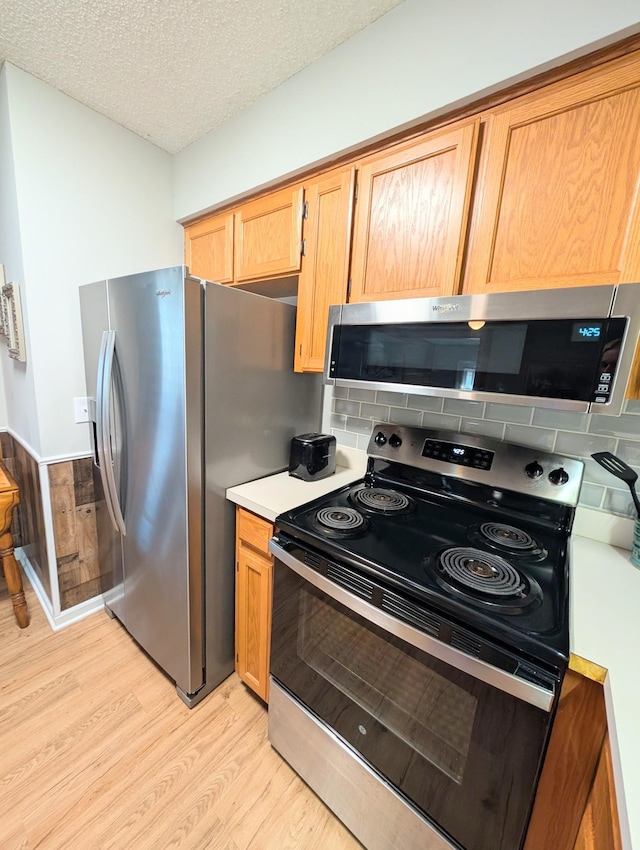 kitchen featuring a textured ceiling, light wood-style flooring, light countertops, appliances with stainless steel finishes, and tasteful backsplash