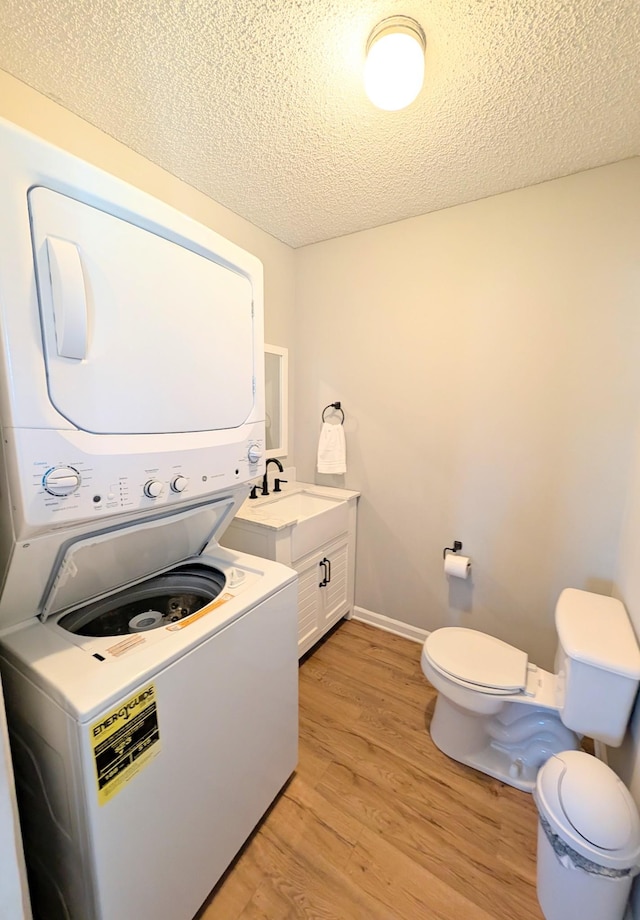 laundry room featuring laundry area, a textured ceiling, light wood-type flooring, stacked washing maching and dryer, and a sink