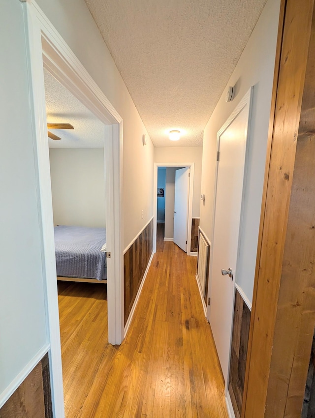 corridor with a textured ceiling and wood-type flooring