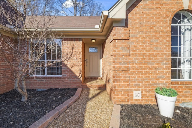 doorway to property featuring brick siding and roof with shingles