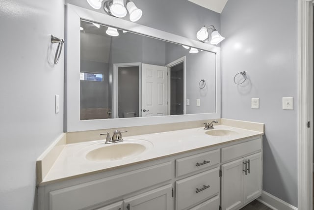 full bathroom featuring double vanity, toilet, baseboards, and a sink