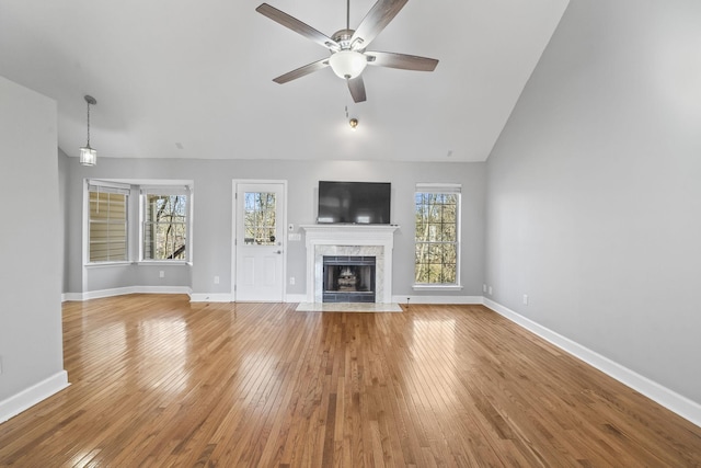 unfurnished living room with a ceiling fan, hardwood / wood-style flooring, a high end fireplace, baseboards, and vaulted ceiling