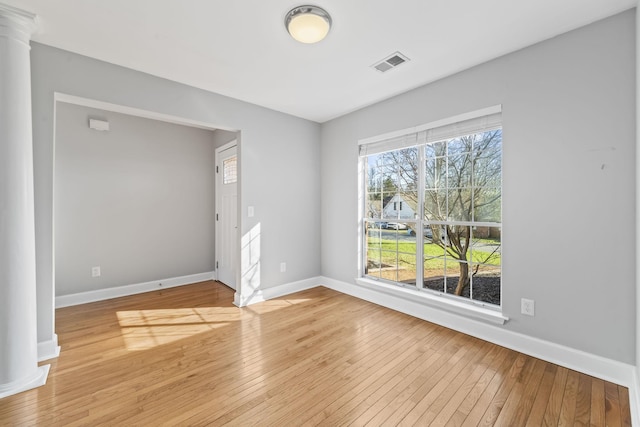 unfurnished room with decorative columns, baseboards, visible vents, and light wood finished floors