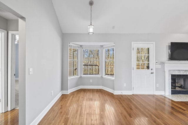 unfurnished living room with a high end fireplace, vaulted ceiling, baseboards, and hardwood / wood-style flooring