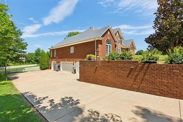 view of property exterior featuring a garage, concrete driveway, brick siding, and fence