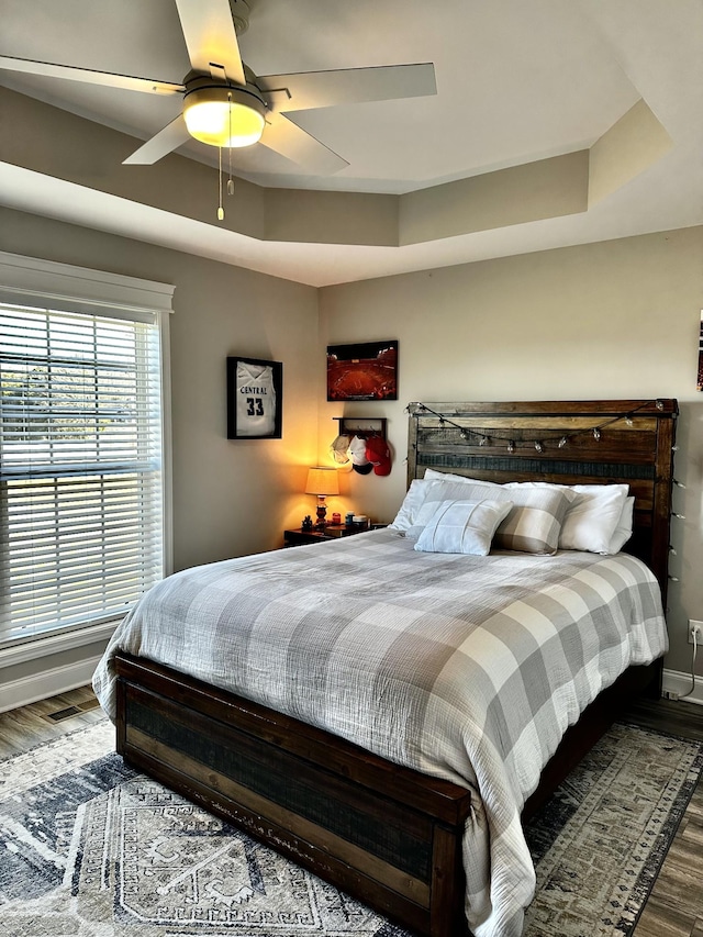 bedroom featuring a tray ceiling, wood finished floors, and baseboards