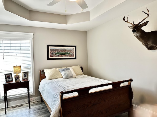 bedroom featuring visible vents, baseboards, a raised ceiling, ceiling fan, and wood finished floors