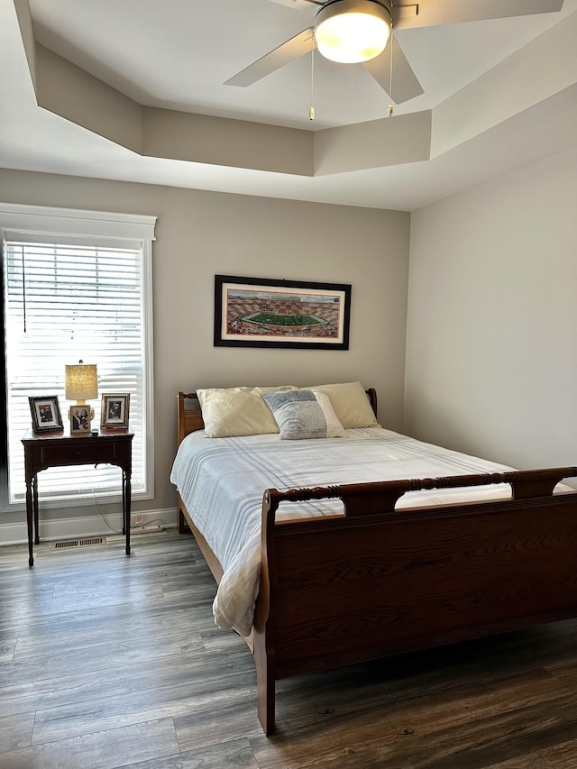 bedroom featuring baseboards, ceiling fan, a tray ceiling, and wood finished floors