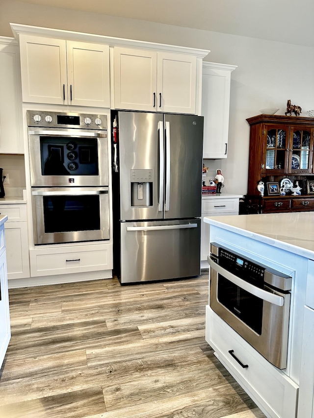 kitchen with light wood finished floors, white cabinetry, appliances with stainless steel finishes, and light countertops