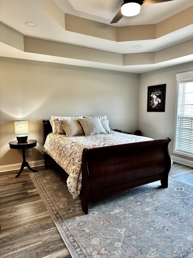 bedroom featuring a ceiling fan, a raised ceiling, baseboards, and wood finished floors