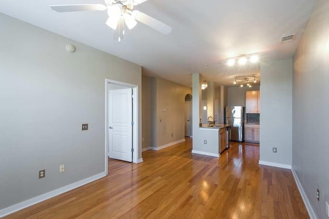 unfurnished room with baseboards, visible vents, arched walkways, light wood-type flooring, and a sink