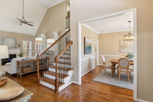 stairway featuring baseboards, wood finished floors, crown molding, a fireplace, and ceiling fan with notable chandelier