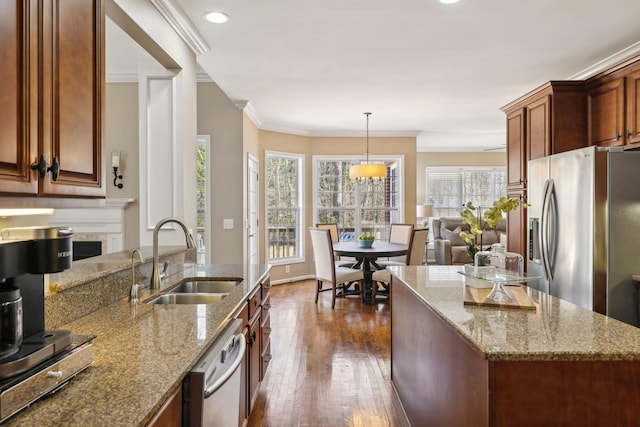 kitchen with appliances with stainless steel finishes, ornamental molding, dark wood-type flooring, a sink, and a high end fireplace