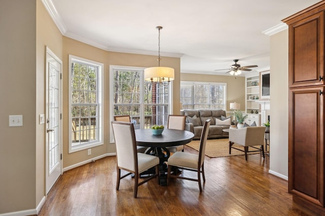 dining space with dark wood-style floors, crown molding, baseboards, and ceiling fan with notable chandelier