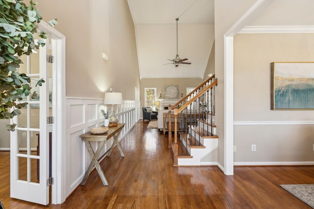 foyer entrance featuring a decorative wall, wood finished floors, a ceiling fan, stairway, and wainscoting