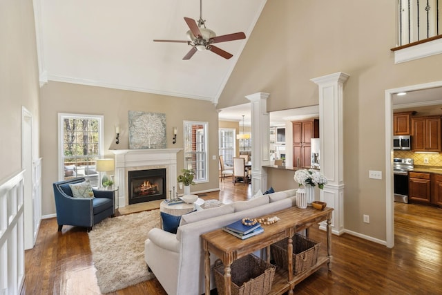 living room with dark wood-style floors, a tiled fireplace, decorative columns, and crown molding