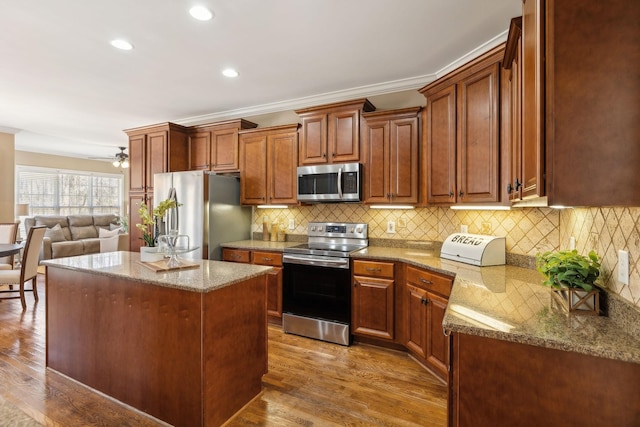 kitchen with stone counters, decorative backsplash, appliances with stainless steel finishes, a kitchen island, and wood finished floors