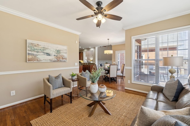 living room featuring ceiling fan with notable chandelier, crown molding, baseboards, and wood finished floors