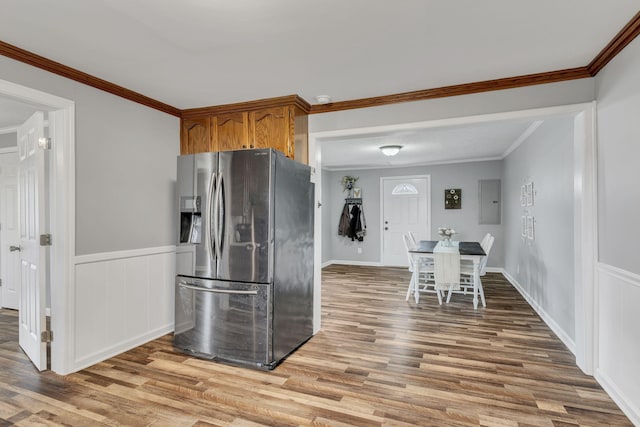 kitchen featuring a wainscoted wall, crown molding, electric panel, light wood-type flooring, and stainless steel fridge